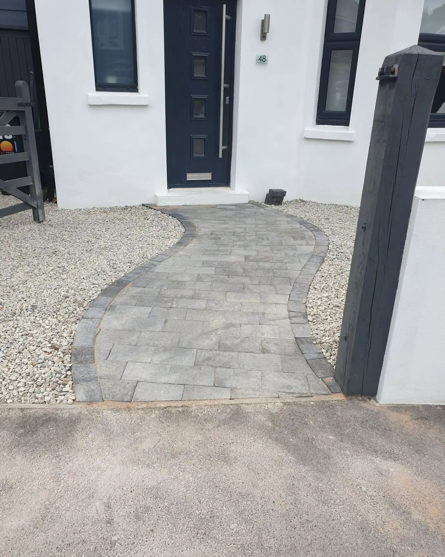 Curved grey block-paved path with charcoal edging through a gravel front garden