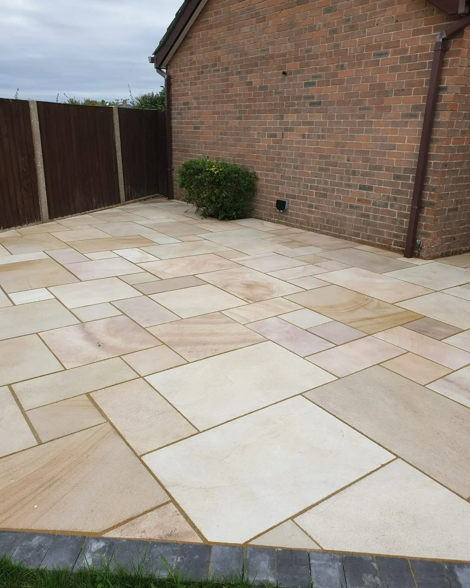 Buff Indian sandstone patio laid against a brick house wall