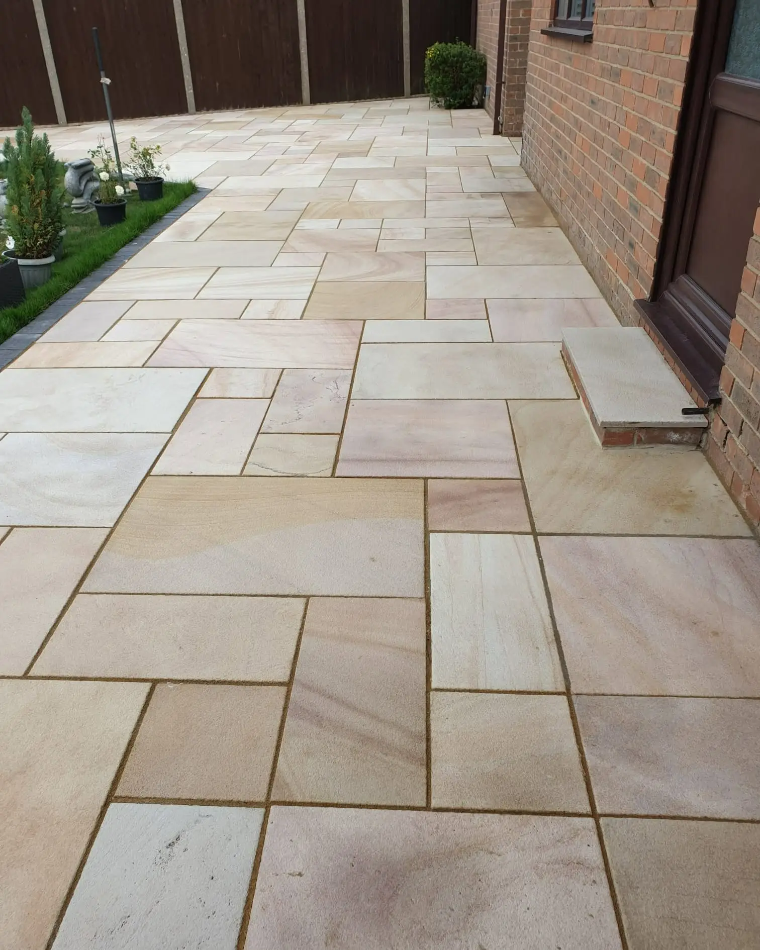 Sandstone patio running along the side of a brick house with a lawn and charcoal edging