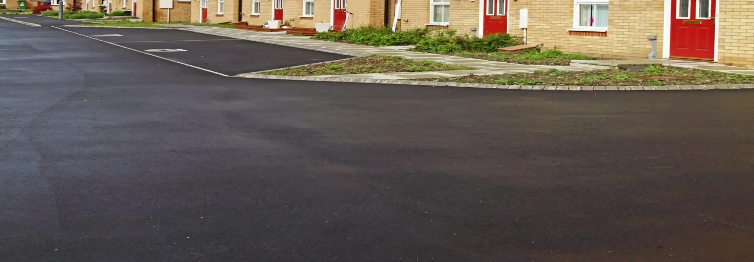 Newly laid tarmac surface with fresh kerbs in front of a row of houses
